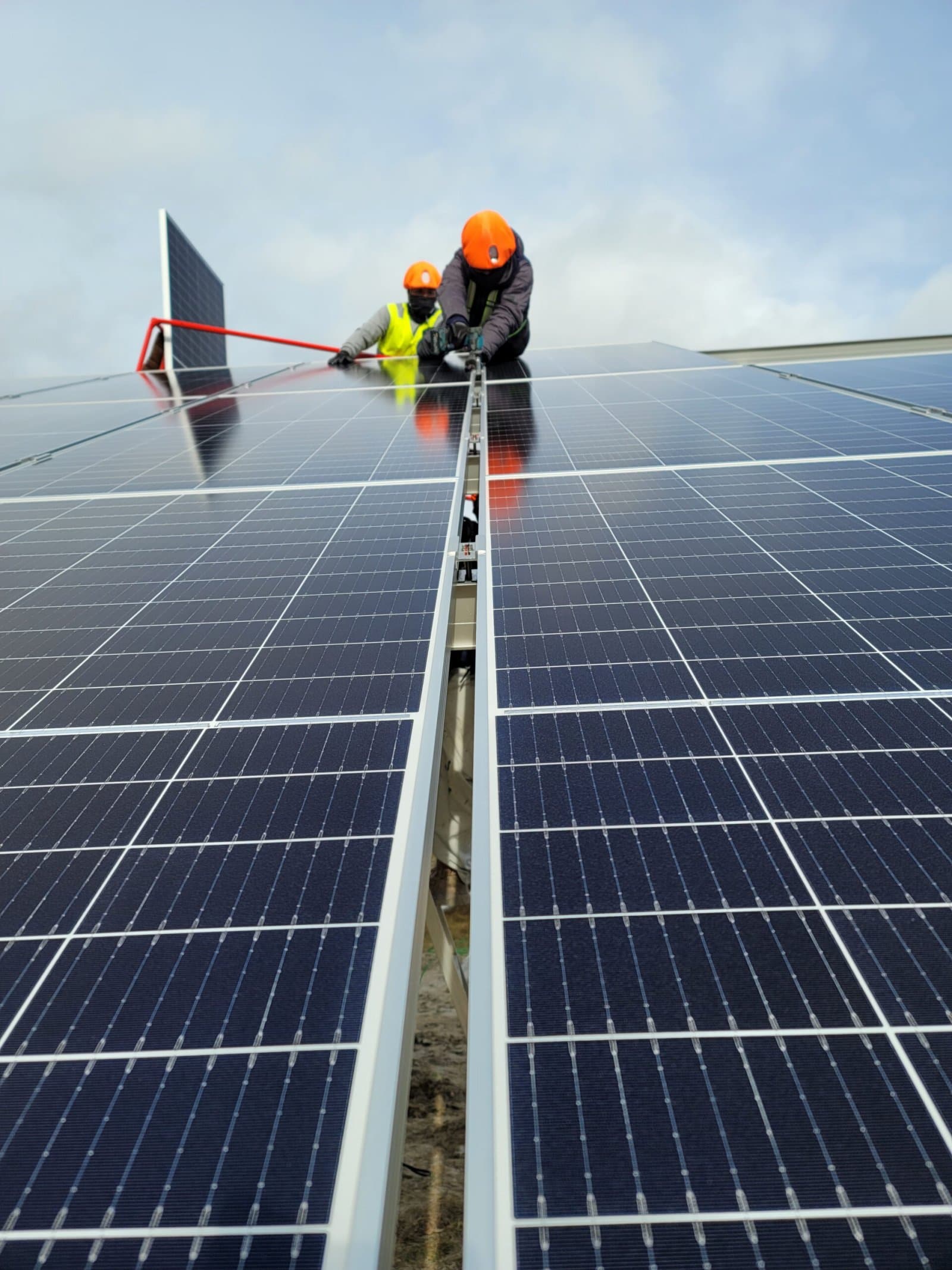 Dos técnicos con casco y chaleco alineando un módulo fotovoltaico sobre estructura metálica